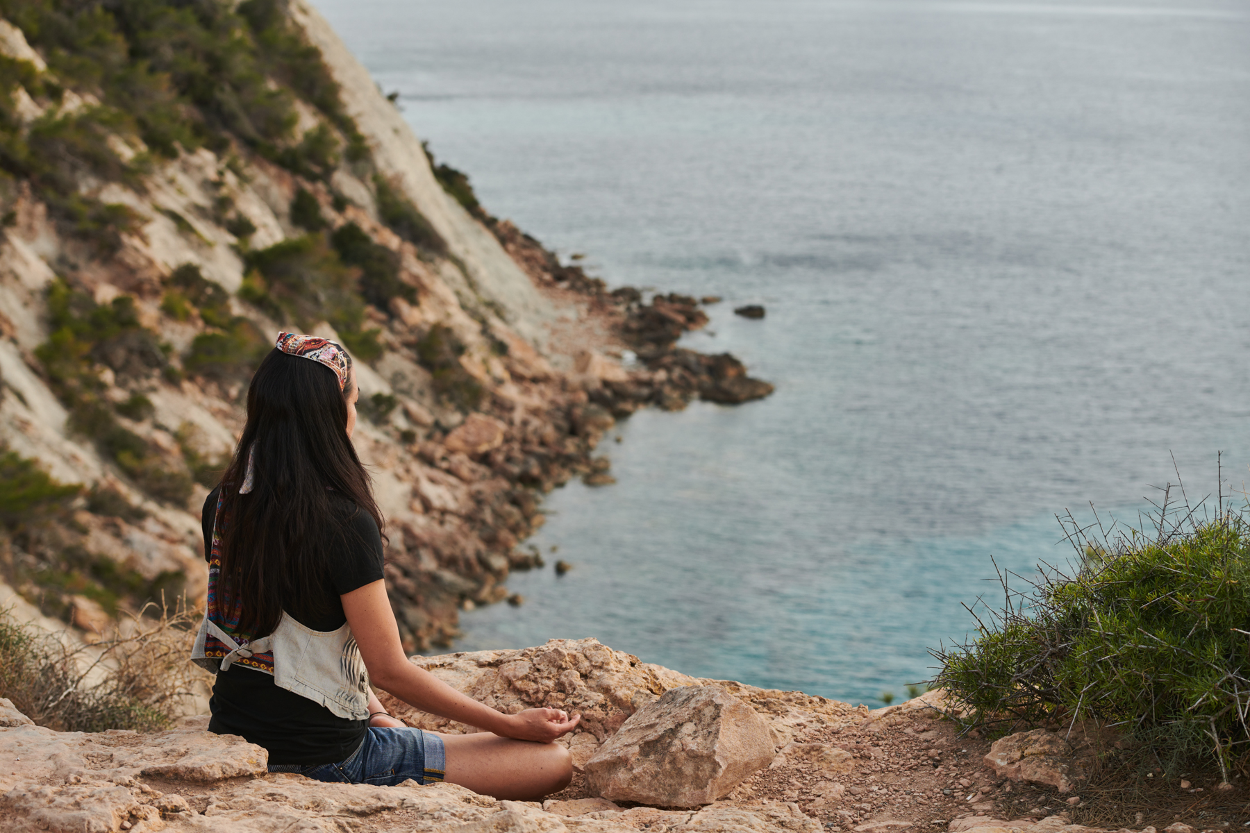 Woman meditating on a rocky cliff overlooking the ocean.