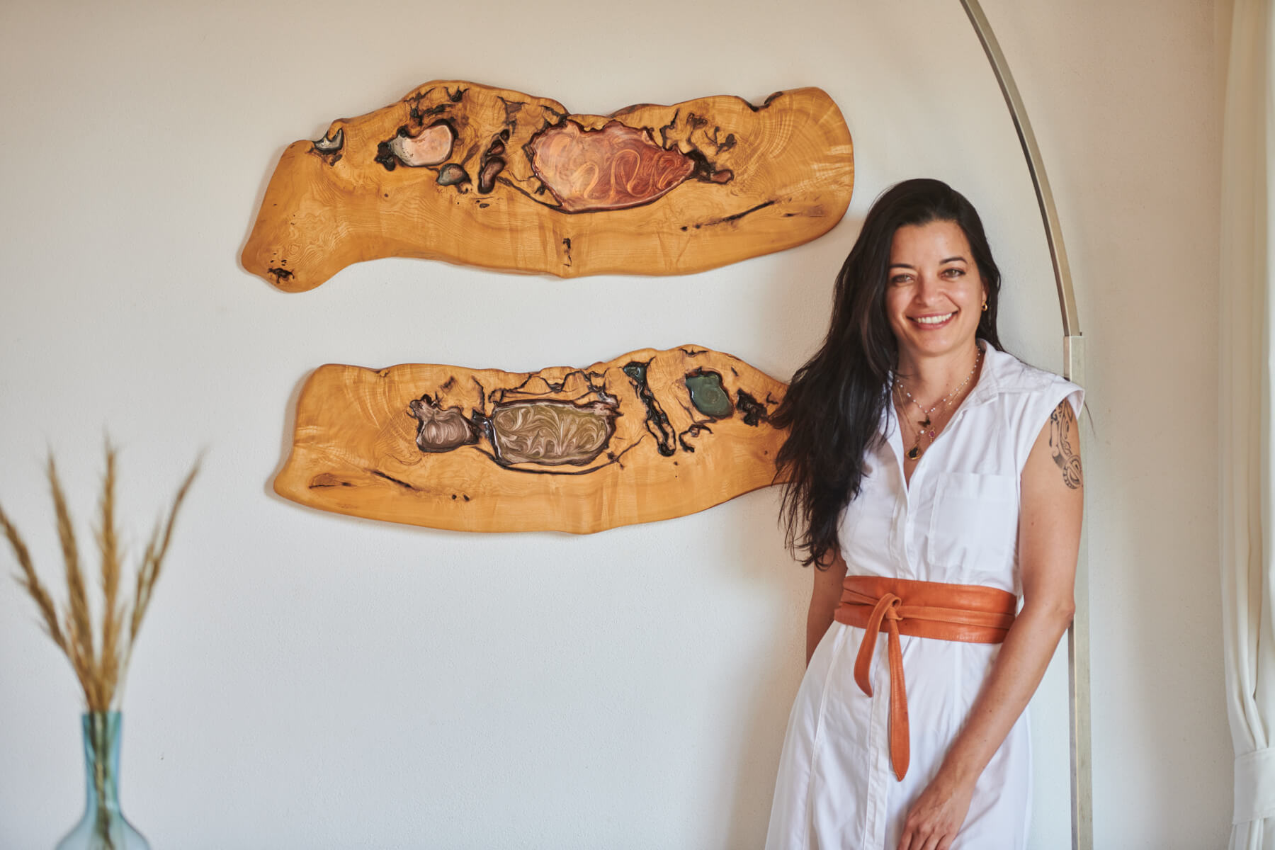 Woman in a white dress standing next to wooden wall art with abstract designs.
