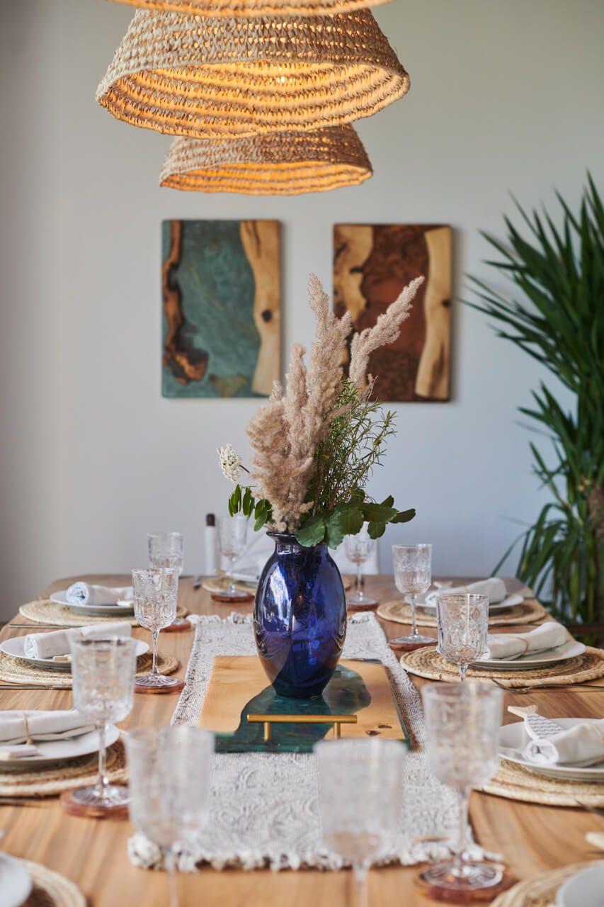 Dining table with blue vase centerpiece, crystal glasses, and woven lampshades