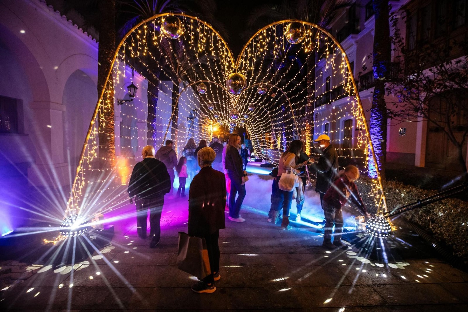 People walking under an archway of golden lights and decorations.